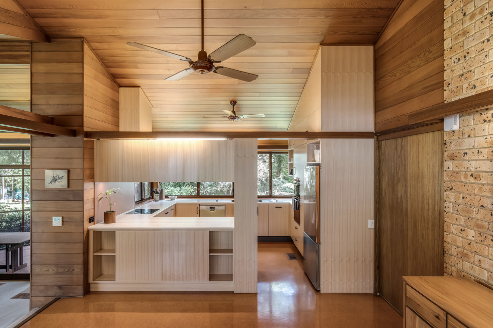Mid-sized contemporary u-shaped eat-in kitchen in Sydney with a drop-in sink, flat-panel cabinets, light wood cabinets, laminate benchtops, orange splashback, glass sheet splashback, stainless steel appliances, cork floors, a peninsula, brown floor, white benchtop and timber.