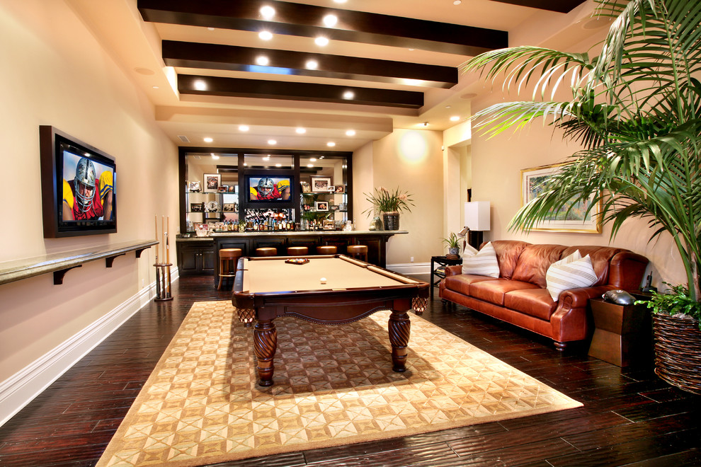 This is an example of a large tropical enclosed family room in Orange County with beige walls, a home bar, dark hardwood floors and a built-in media wall.
