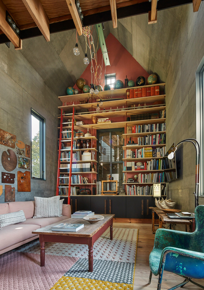 Photo of an industrial living room in New York with a library, grey walls, medium hardwood floors, a wall-mounted tv, brown floor and vaulted.