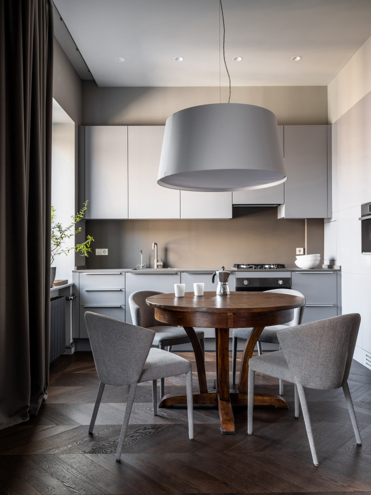 Mid-sized contemporary l-shaped eat-in kitchen in Moscow with a single-bowl sink, flat-panel cabinets, grey cabinets, quartz benchtops, grey splashback, engineered quartz splashback, black appliances, dark hardwood floors, no island, brown floor and grey benchtop.