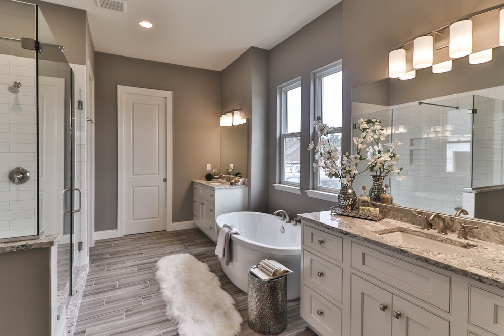 Photo of a mid-sized transitional master bathroom in St Louis with shaker cabinets, dark wood cabinets, a freestanding tub, an alcove shower, a two-piece toilet, white tile, porcelain tile, beige walls, vinyl floors, an undermount sink, granite benchtops, grey floor and a hinged shower door.