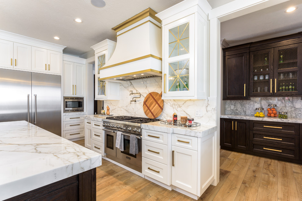 Photo of a large transitional single-wall separate kitchen in Salt Lake City with a farmhouse sink, shaker cabinets, white cabinets, marble benchtops, grey splashback, marble splashback, stainless steel appliances, medium hardwood floors, brown floor, grey benchtop and multiple islands.
