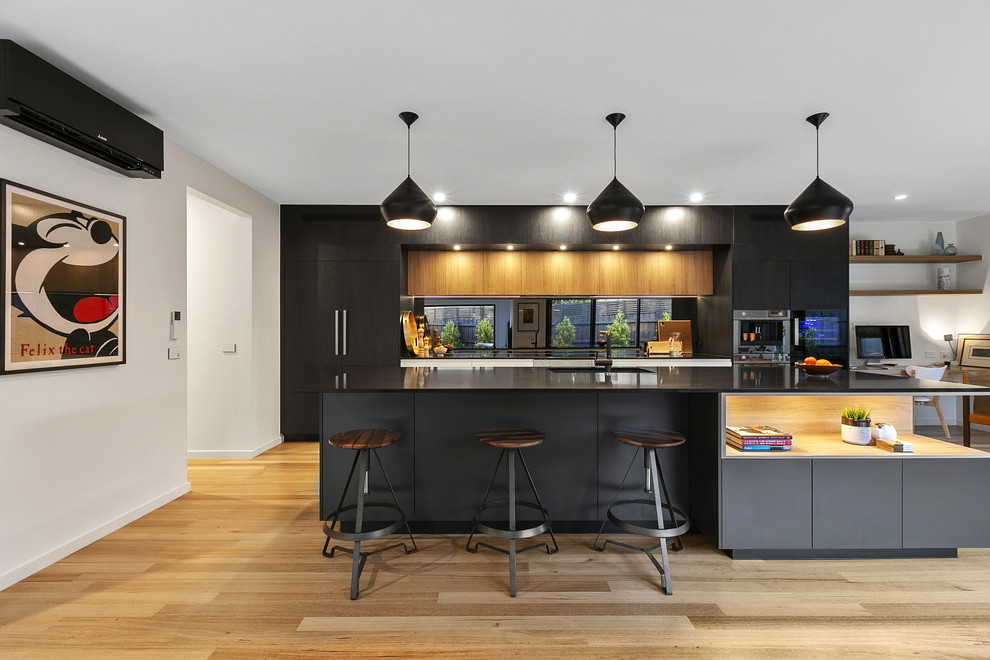Design ideas for a contemporary single-wall kitchen in Melbourne with an undermount sink, flat-panel cabinets, black cabinets, mirror splashback, black appliances, medium hardwood floors, with island, brown floor and black benchtop.
