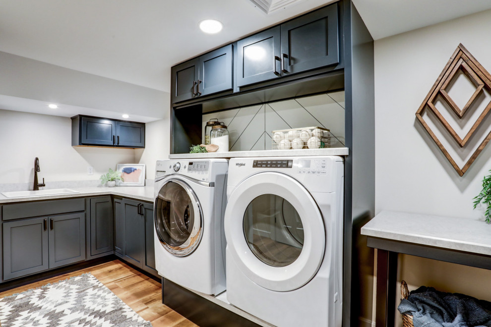Idéer för en stor klassisk grå l-formad tvättstuga enbart för tvätt, med en nedsänkt diskho, luckor med infälld panel, blå skåp, laminatbänkskiva, vita väggar, vinylgolv, en tvättmaskin och torktumlare bredvid varandra och brunt golv