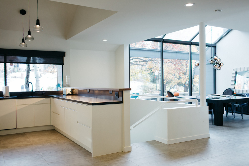 Design ideas for a mid-sized modern u-shaped open plan kitchen in Salt Lake City with a double-bowl sink, flat-panel cabinets, white cabinets, zinc benchtops, brown splashback, mosaic tile splashback, black appliances, ceramic floors and with island.