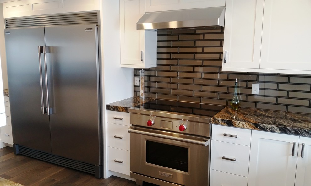 Inspiration for a large modern galley eat-in kitchen in Salt Lake City with an undermount sink, shaker cabinets, white cabinets, granite benchtops, metallic splashback, glass tile splashback, stainless steel appliances, dark hardwood floors, a peninsula, brown floor and green benchtop.