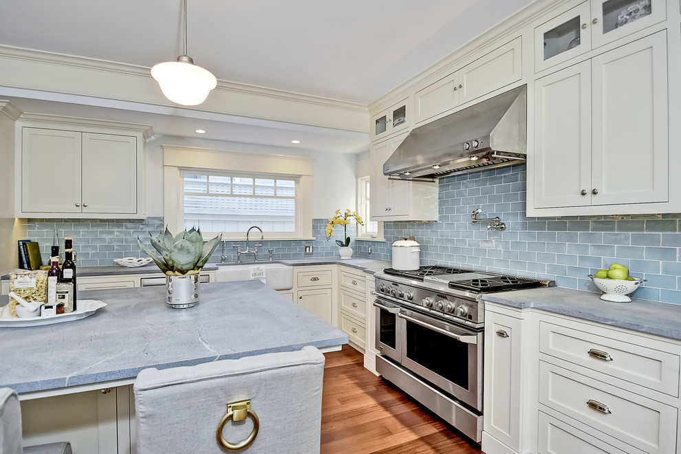 Photo of a large transitional l-shaped open plan kitchen in San Diego with a farmhouse sink, shaker cabinets, white cabinets, concrete benchtops, blue splashback, ceramic splashback, stainless steel appliances, medium hardwood floors and with island.