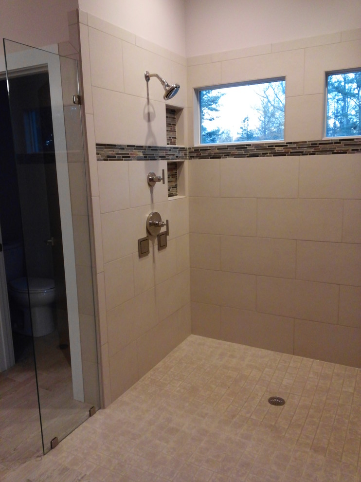 This is an example of a large contemporary master bathroom in Raleigh with flat-panel cabinets, medium wood cabinets, a curbless shower, a two-piece toilet, beige tile, cement tile, porcelain floors, an undermount sink, granite benchtops, an open shower and black benchtops.