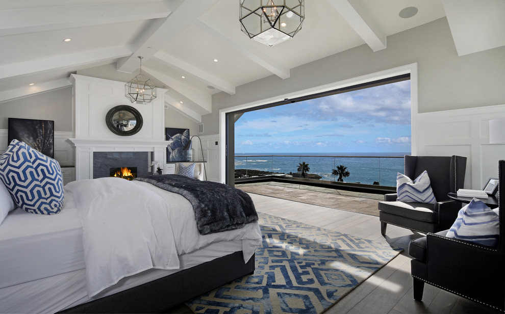 Design ideas for a beach style master bedroom in Orange County with grey walls, a standard fireplace and light hardwood floors.
