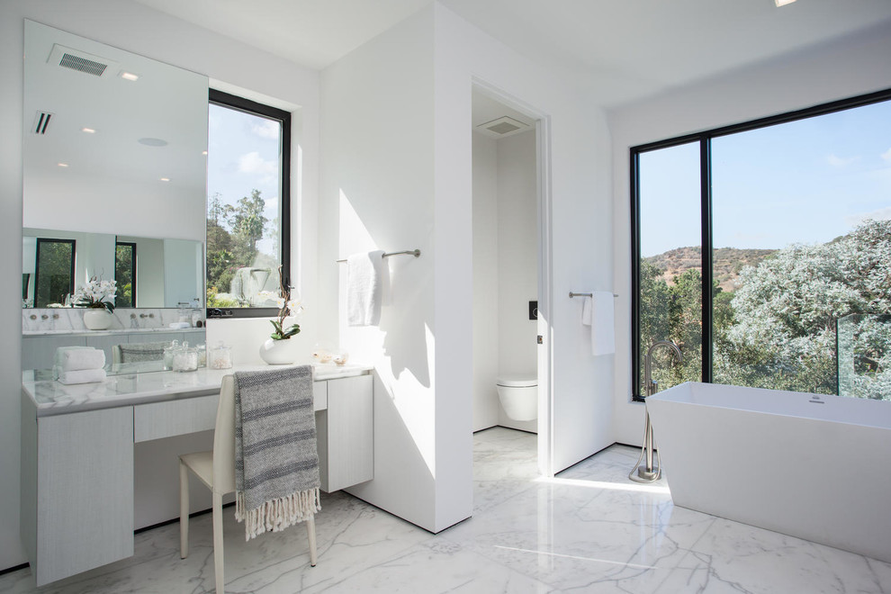 Design ideas for a large modern master bathroom in Los Angeles with flat-panel cabinets, light wood cabinets, a freestanding tub, a curbless shower, a wall-mount toilet, stone slab, white walls, marble floors, an undermount sink, marble benchtops, white tile and an enclosed toilet.