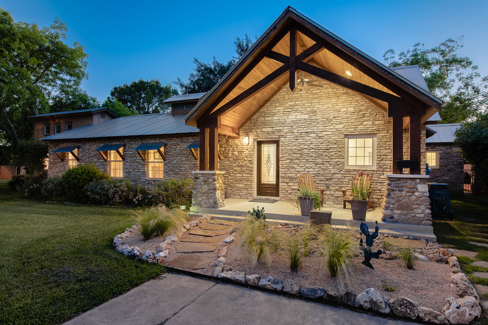 This is an example of a large modern two-storey beige house exterior in Austin with stone veneer, a gambrel roof and a metal roof.