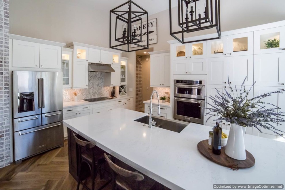 Large traditional l-shaped eat-in kitchen in Phoenix with a farmhouse sink, shaker cabinets, white cabinets, quartzite benchtops, grey splashback, matchstick tile splashback, stainless steel appliances, light hardwood floors, with island and brown floor.