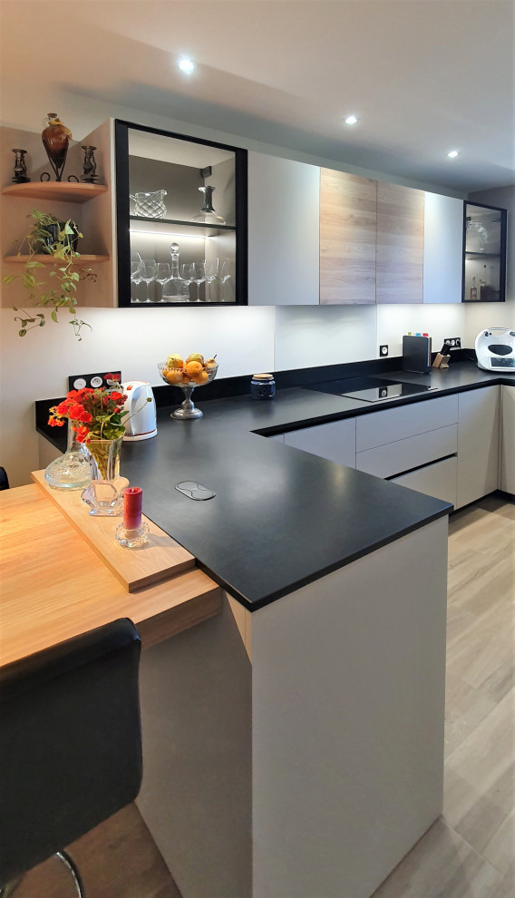 Mid-sized modern single-wall open plan kitchen in Other with an undermount sink, flat-panel cabinets, white cabinets, granite benchtops, black splashback, granite splashback, panelled appliances, laminate floors, with island, beige floor and black benchtop.