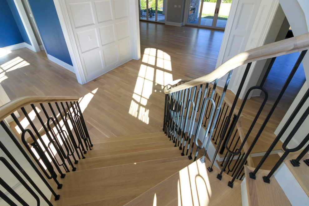 Diseño de escalera curva clásica renovada extra grande con escalones de madera, contrahuellas de madera, barandilla de varios materiales y boiserie