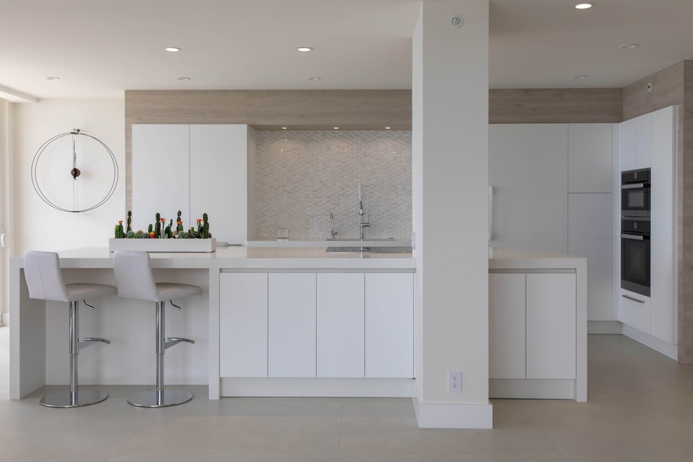 This is an example of a large contemporary l-shaped open plan kitchen in Other with an undermount sink, flat-panel cabinets, white cabinets, quartz benchtops, white splashback, porcelain splashback, stainless steel appliances, porcelain floors, with island, beige floor and white benchtop.