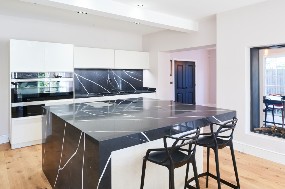 Design ideas for a medium sized contemporary single-wall open plan kitchen in Other with flat-panel cabinets, white cabinets, quartz worktops, black splashback, an island and black worktops.