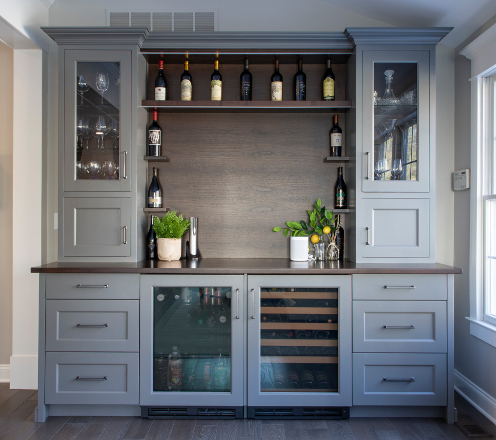 This is an example of a transitional single-wall home bar in Philadelphia with recessed-panel cabinets, grey cabinets, wood benchtops, timber splashback, dark hardwood floors and brown benchtop.