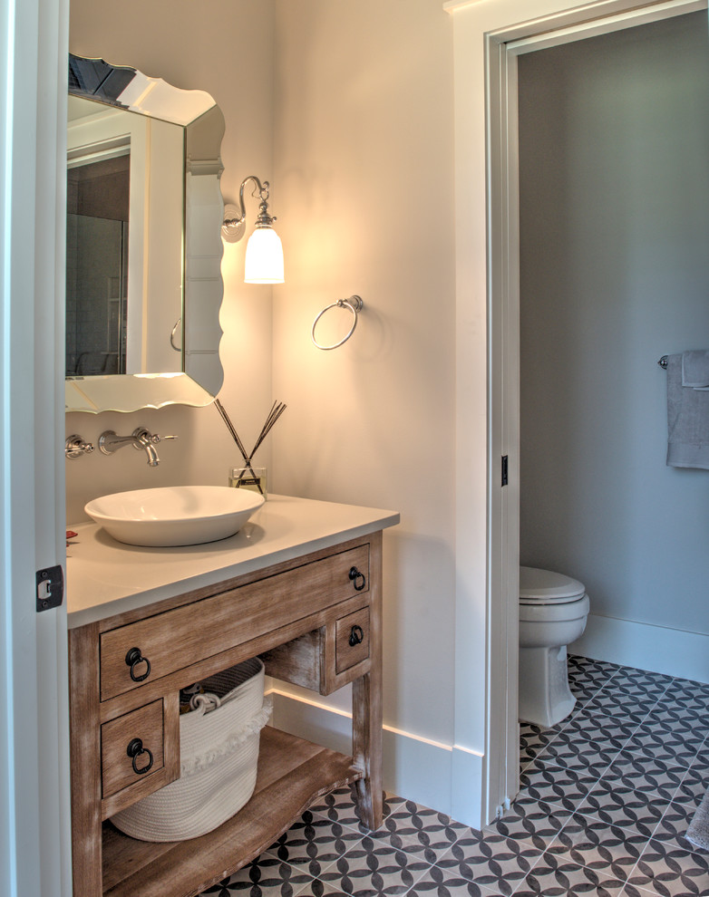 This is an example of a mid-sized transitional powder room in Philadelphia with beaded inset cabinets, distressed cabinets, a two-piece toilet, grey walls, cement tiles, a vessel sink, solid surface benchtops, multi-coloured floor and white benchtops.