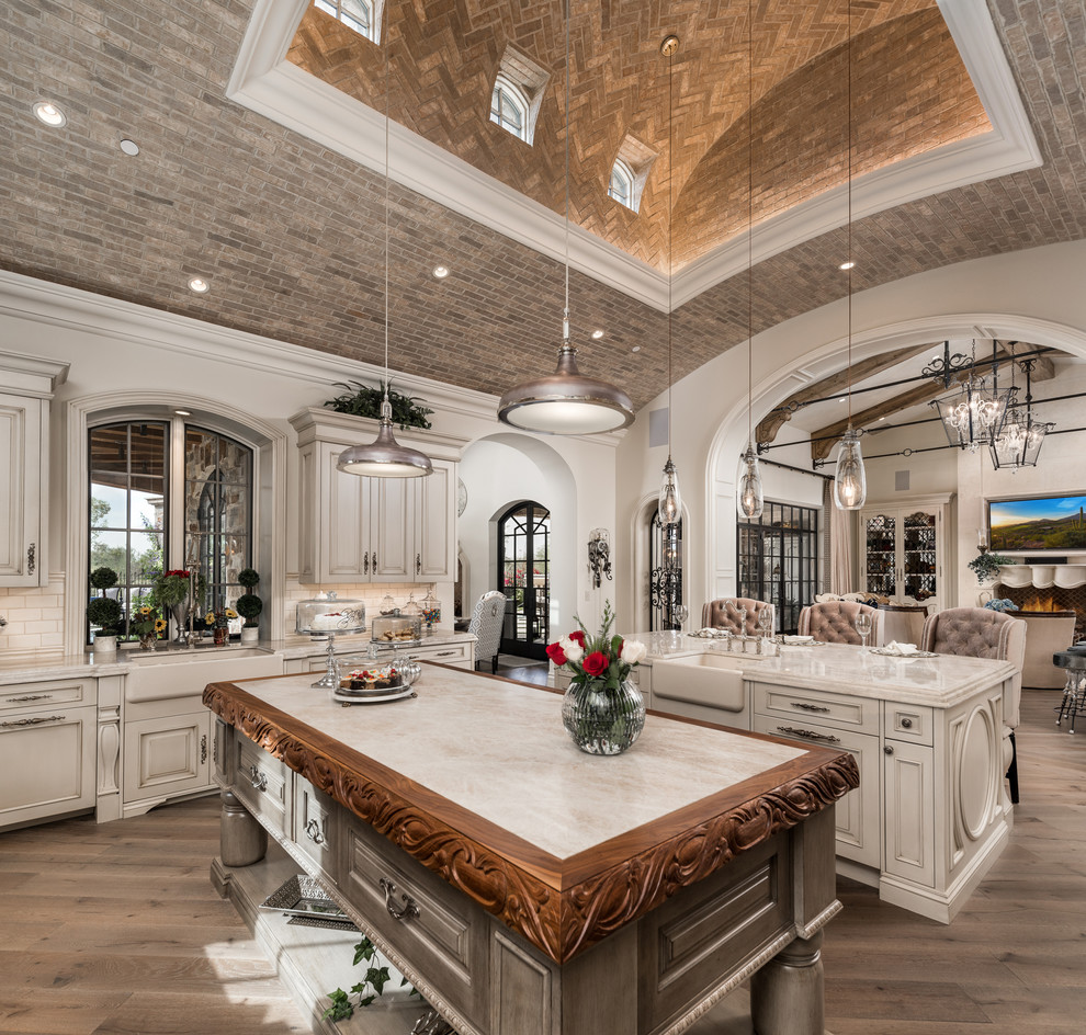 Example of a huge transitional u-shaped brown floor, dark wood floor and vaulted ceiling enclosed kitchen design in Phoenix with a farmhouse sink, raised-panel cabinets, light wood cabinets, quartzite countertops, two islands, multicolored backsplash, porcelain backsplash, beige countertops and paneled appliances