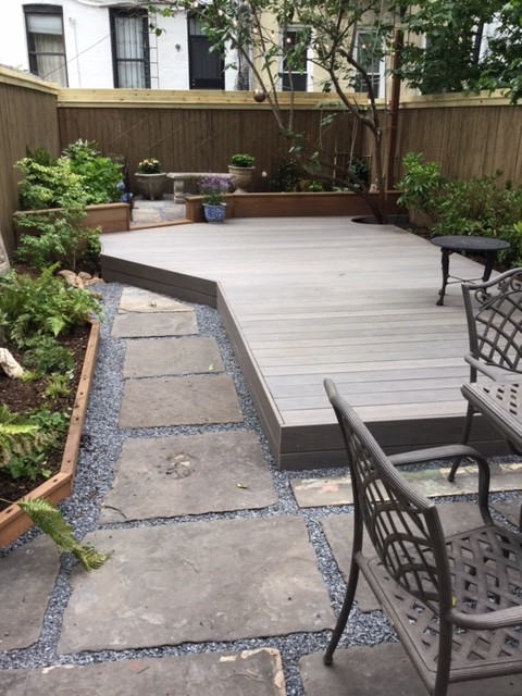 Small eclectic backyard shaded xeriscape in New York with natural stone pavers for summer.