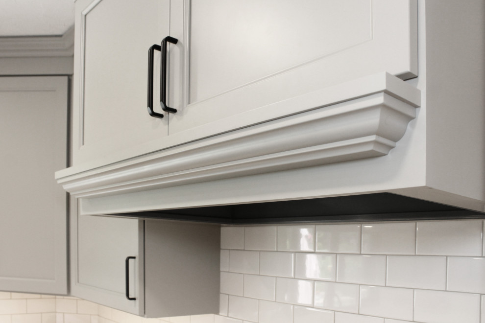 Large transitional u-shaped light wood floor and brown floor enclosed kitchen photo in Boston with a double-bowl sink, shaker cabinets, gray cabinets, quartz countertops, white backsplash, porcelain backsplash, black appliances, an island and white countertops