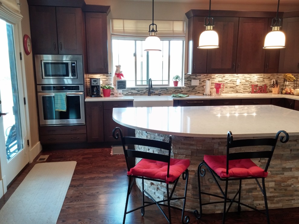 This is an example of a modern u-shaped eat-in kitchen in Denver with a farmhouse sink, shaker cabinets, dark wood cabinets, quartzite benchtops, multi-coloured splashback, glass tile splashback, stainless steel appliances, dark hardwood floors and with island.