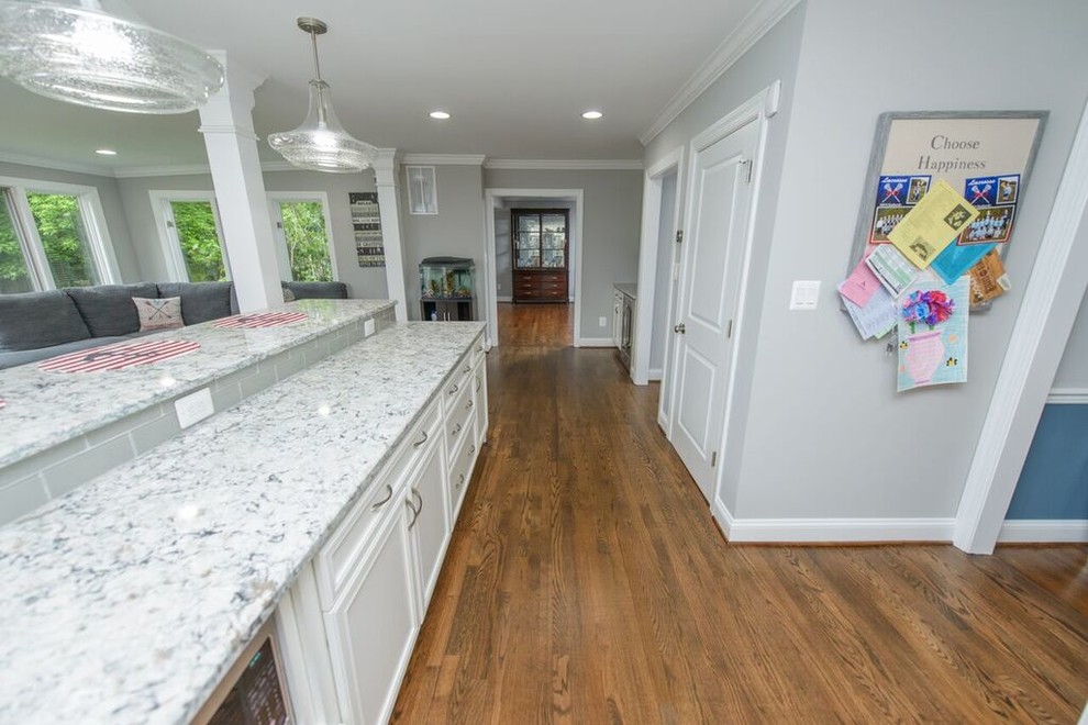 Eat-in kitchen - transitional l-shaped medium tone wood floor eat-in kitchen idea in Baltimore with a farmhouse sink, beaded inset cabinets, white cabinets, granite countertops, gray backsplash, glass tile backsplash, stainless steel appliances and an island