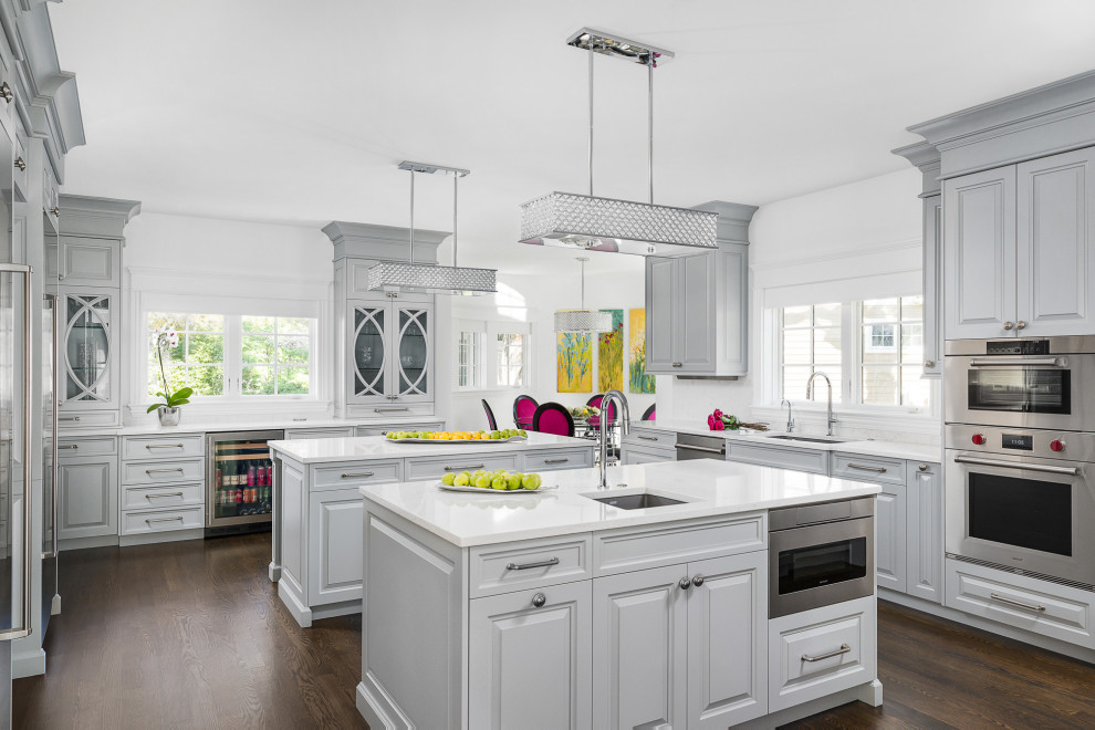 Design ideas for a large transitional u-shaped eat-in kitchen in Chicago with an undermount sink, grey cabinets, quartzite benchtops, white splashback, stainless steel appliances, dark hardwood floors, multiple islands, brown floor, white benchtop and raised-panel cabinets.