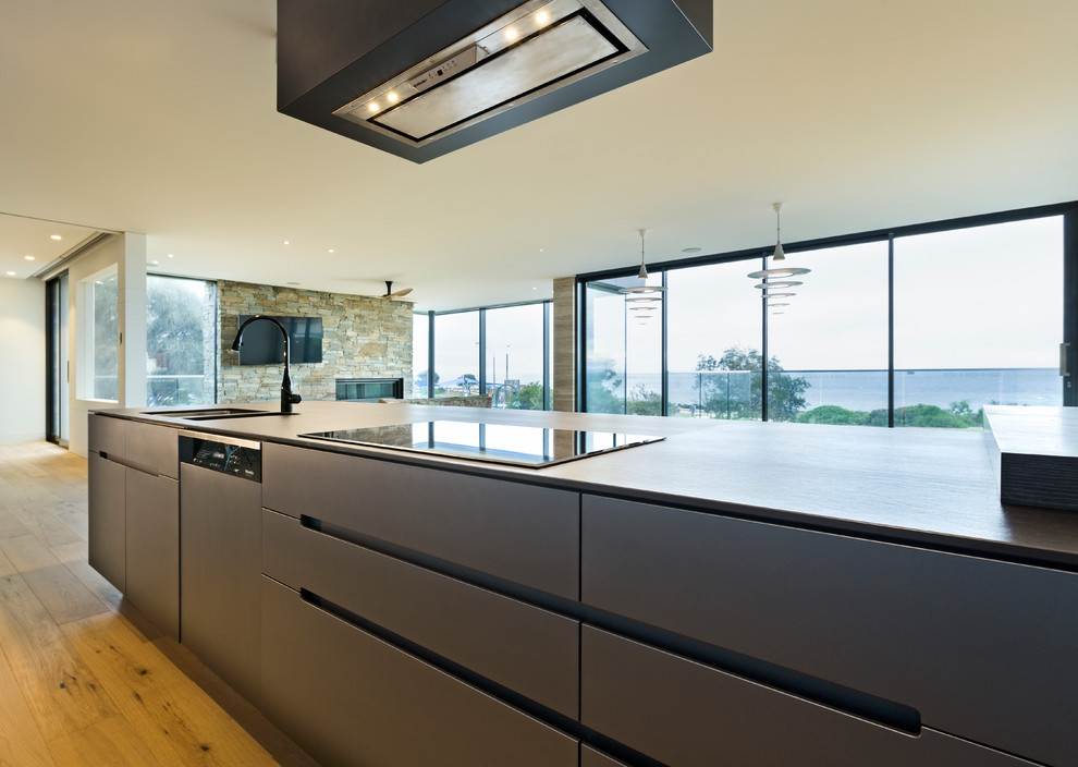 Large contemporary galley kitchen in Melbourne with a double-bowl sink, flat-panel cabinets, dark wood cabinets, stainless steel appliances, light hardwood floors and with island.