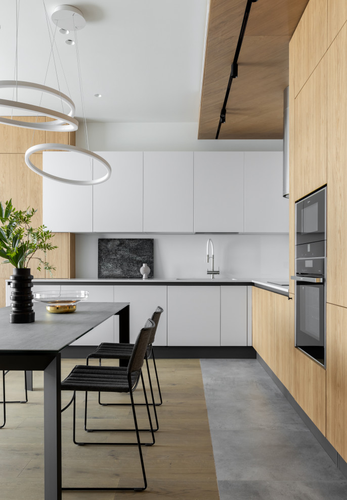 Photo of a large contemporary l-shaped eat-in kitchen in Moscow with an undermount sink, flat-panel cabinets, quartz benchtops, glass sheet splashback, black appliances, porcelain floors, no island, grey floor, grey benchtop and wood.