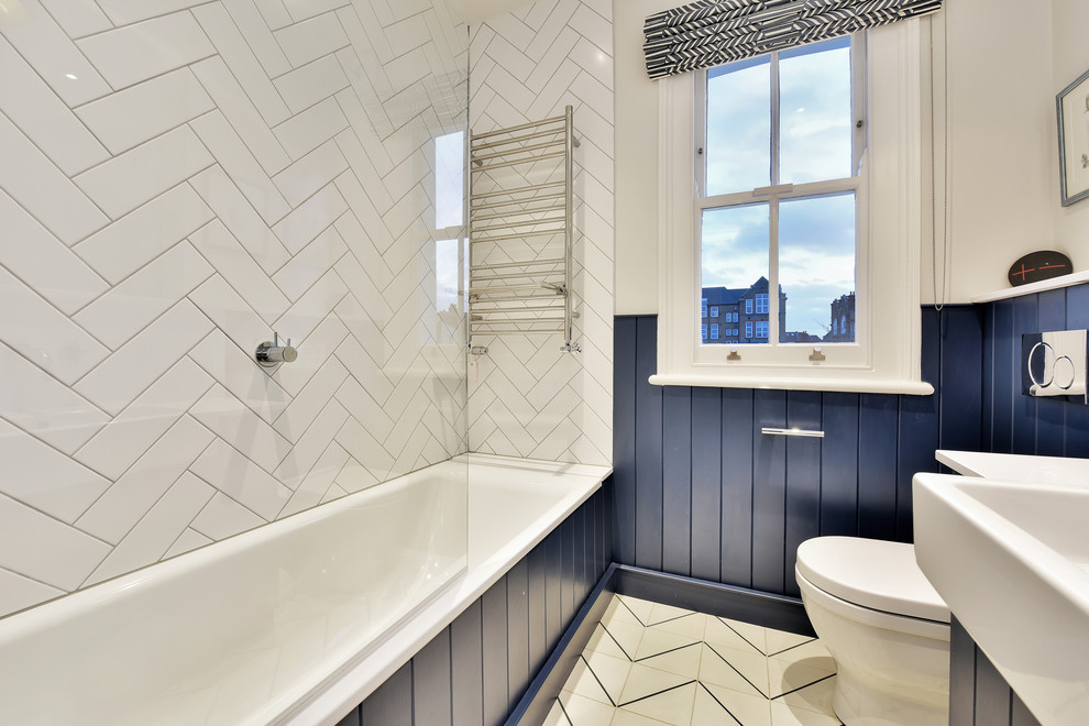 Transitional bathroom in London with blue cabinets, a drop-in tub, white tile, white walls and multi-coloured floor.