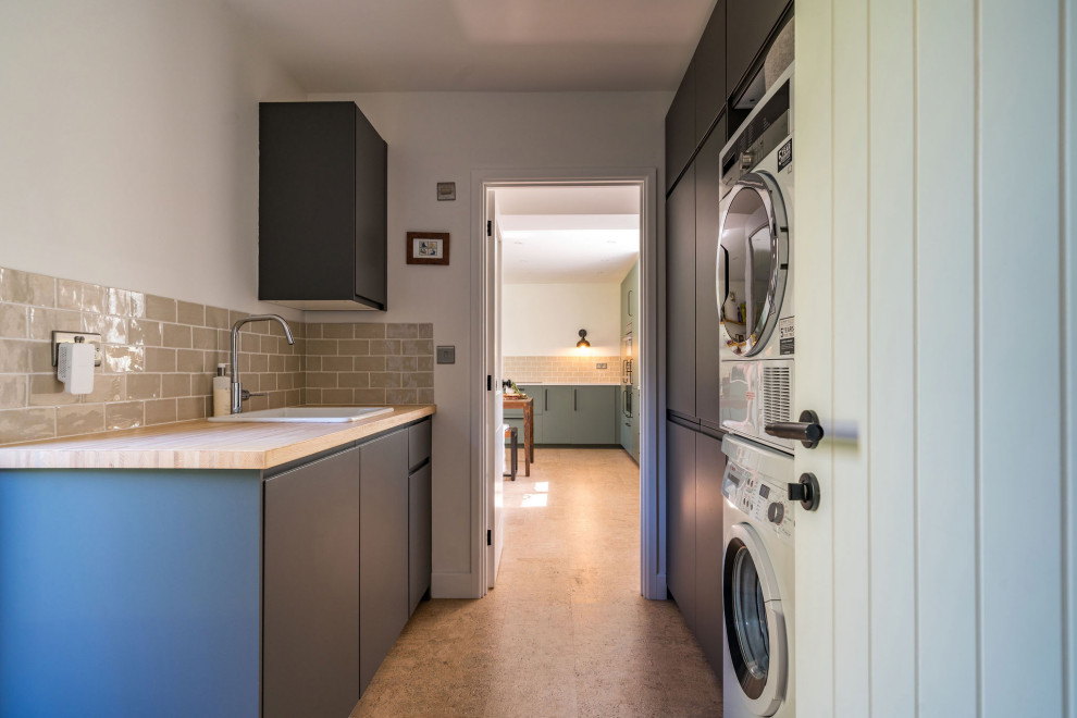 Mid-sized modern galley dedicated laundry room in Oxfordshire with an integrated sink, flat-panel cabinets, grey cabinets, wood benchtops, beige splashback, ceramic splashback, white walls, cork floors, beige floor and beige benchtop.