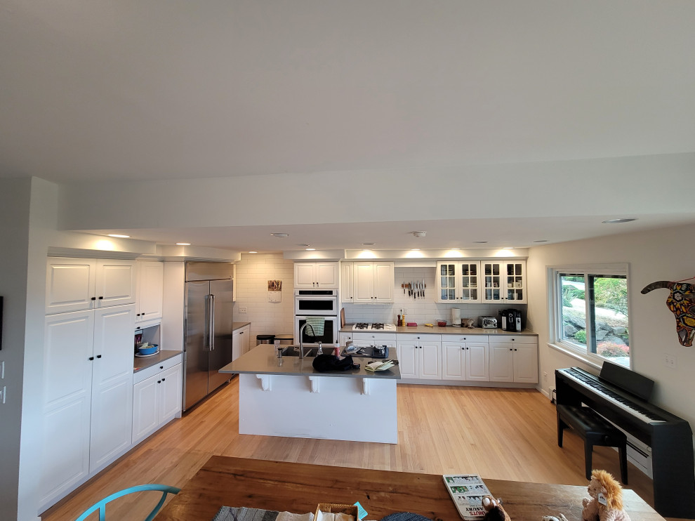 Photo of a large contemporary galley kitchen/diner in Seattle with a double-bowl sink, beaded cabinets, brown cabinets, marble worktops, grey splashback, marble splashback, white appliances, painted wood flooring, multiple islands, brown floors, grey worktops and a coffered ceiling.