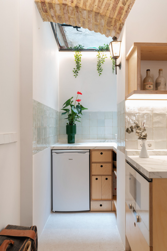 Photo of a small midcentury single-wall open plan kitchen in Valencia with an undermount sink, flat-panel cabinets, light wood cabinets, tile benchtops, grey splashback, porcelain splashback, panelled appliances, ceramic floors, beige floor, white benchtop and exposed beam.