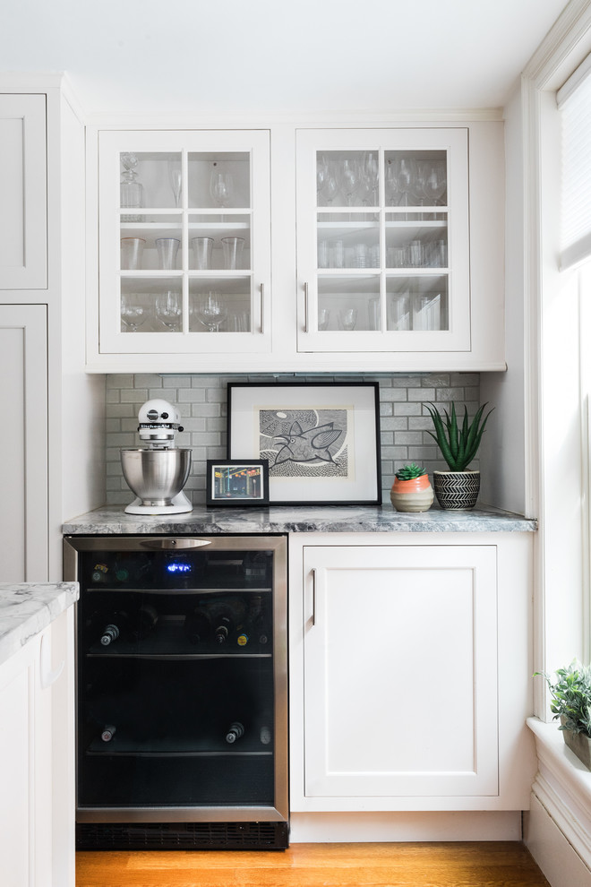 Design ideas for a transitional home bar in Boston with glass-front cabinets, white cabinets, white splashback, subway tile splashback, medium hardwood floors and multi-coloured benchtop.