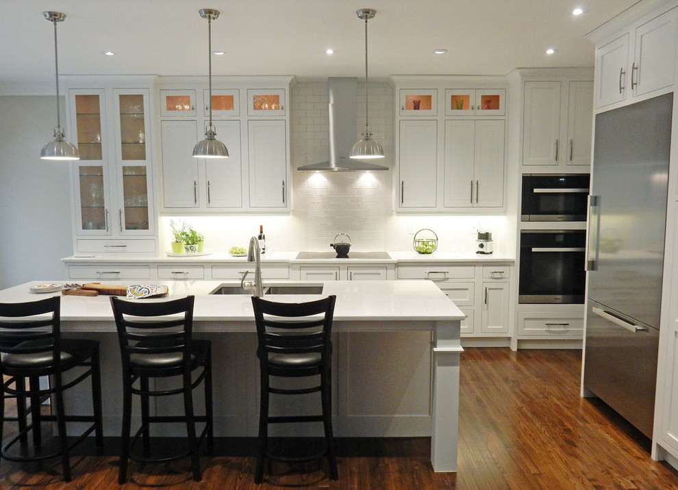 Open concept kitchen - mid-sized transitional l-shaped dark wood floor and brown floor open concept kitchen idea with a double-bowl sink, beaded inset cabinets, white cabinets, quartz countertops, white backsplash, glass tile backsplash, stainless steel appliances, an island and white countertops