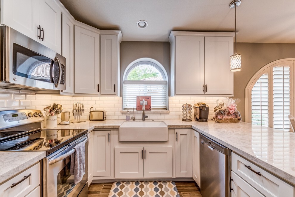 Example of a mid-sized transitional u-shaped porcelain tile and beige floor eat-in kitchen design in Phoenix with a farmhouse sink, shaker cabinets, white cabinets, quartz countertops, white backsplash, subway tile backsplash, stainless steel appliances and white countertops