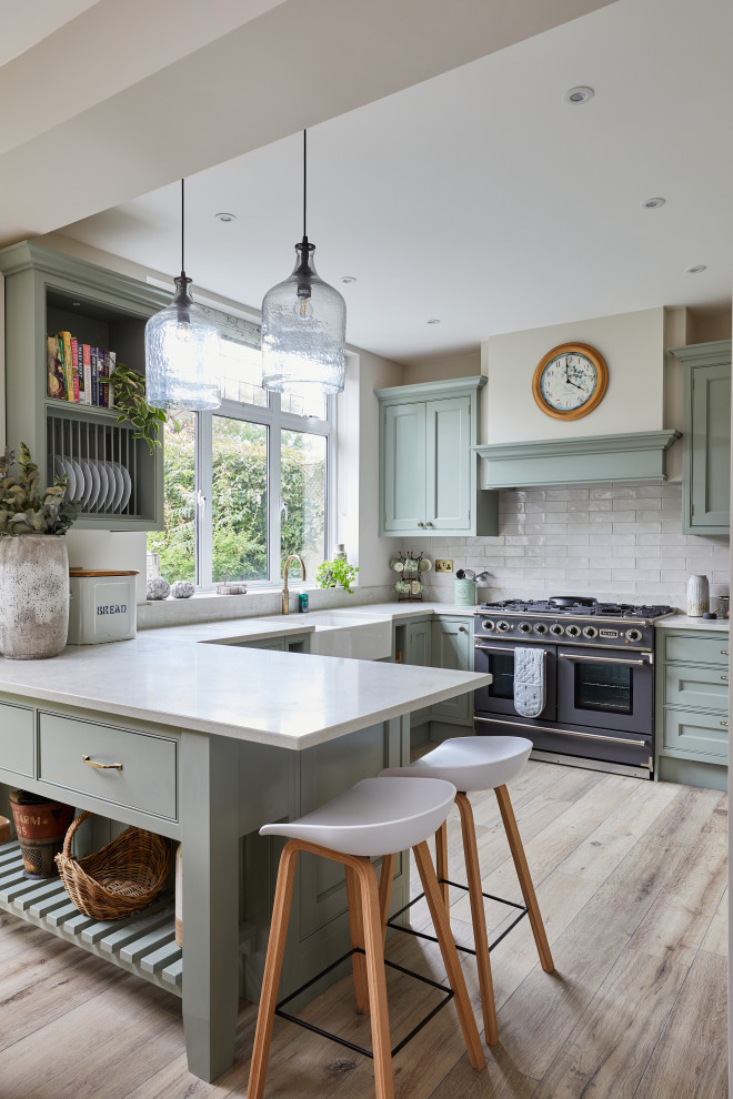 Photo of a traditional u-shaped kitchen in London with a farmhouse sink, beaded inset cabinets, turquoise cabinets, white splashback, subway tile splashback, coloured appliances, light hardwood floors, a peninsula, beige floor and white benchtop.