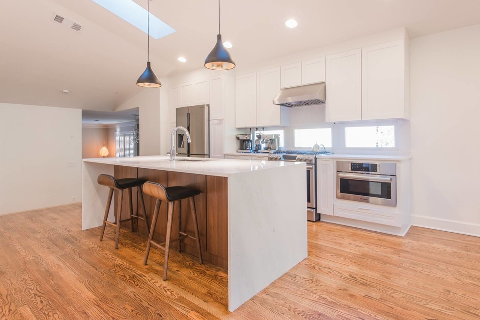 Inspiration for a mid-sized transitional single-wall light wood floor open concept kitchen remodel in Atlanta with a double-bowl sink, recessed-panel cabinets, white cabinets, marble countertops, white backsplash, subway tile backsplash, stainless steel appliances and an island