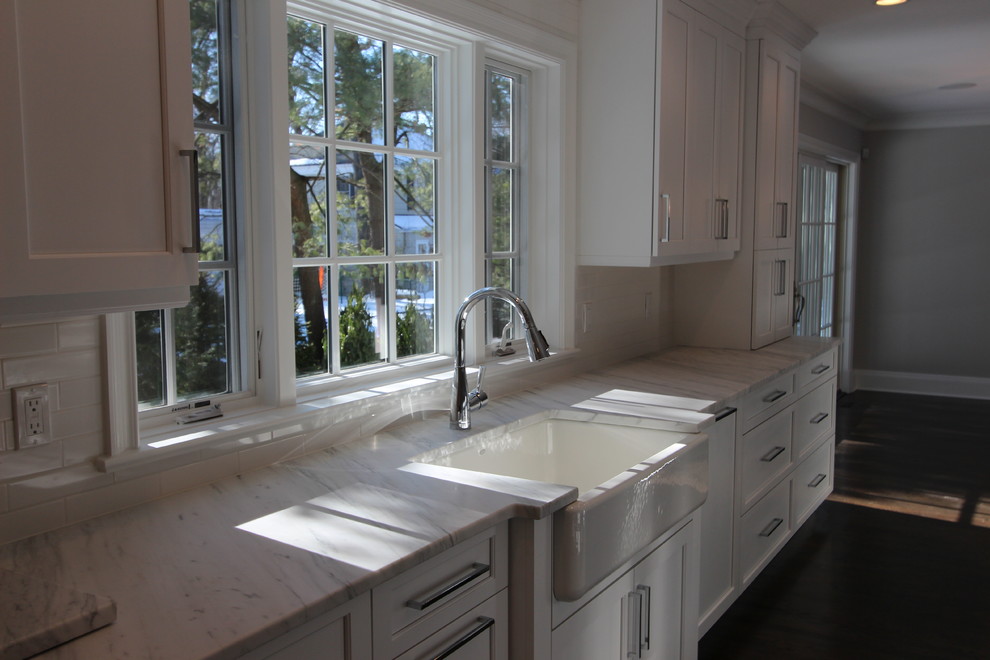 Large transitional l-shaped dark wood floor eat-in kitchen photo in New York with a farmhouse sink, shaker cabinets, white cabinets, marble countertops, white backsplash, subway tile backsplash, stainless steel appliances and an island