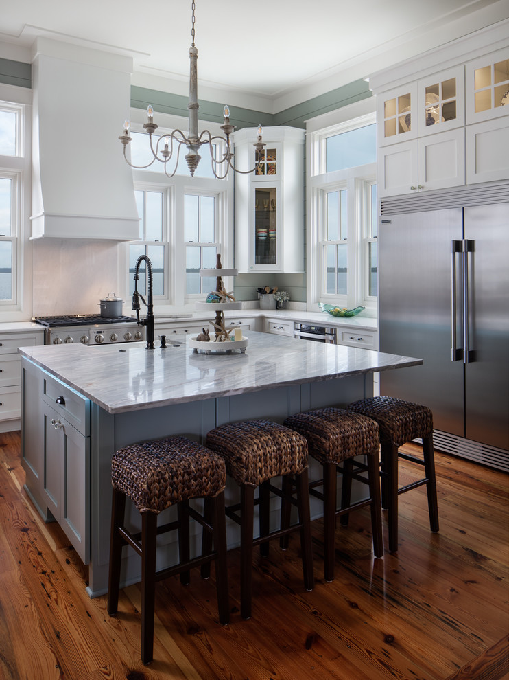 Photo of a beach style kitchen in New Orleans with a farmhouse sink, shaker cabinets, white cabinets, stainless steel appliances, medium hardwood floors, with island, brown floor and white benchtop.