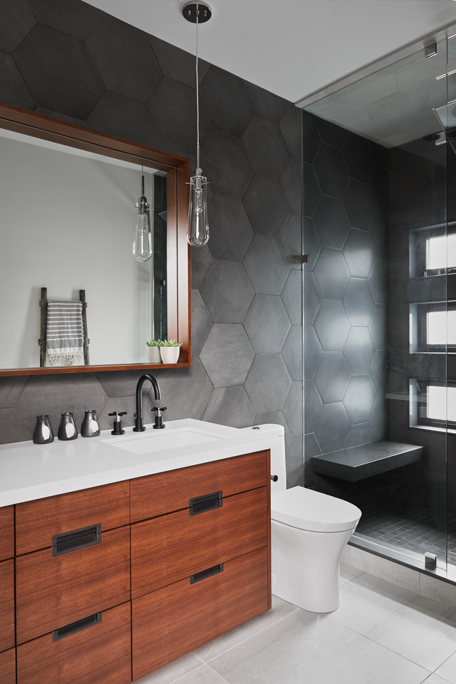 Inspiration for a mid-sized eclectic master wet room bathroom in Toronto with flat-panel cabinets, medium wood cabinets, black tile, porcelain tile, white walls, porcelain floors, an undermount sink, solid surface benchtops, grey floor and a hinged shower door.
