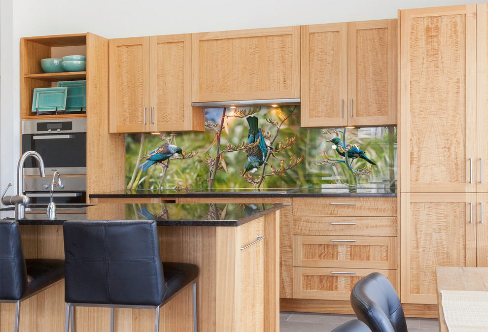 Inspiration for a mid-sized tropical eat-in kitchen in Auckland with a single-bowl sink, shaker cabinets, medium wood cabinets, granite benchtops, green splashback, glass sheet splashback, stainless steel appliances, ceramic floors and with island.