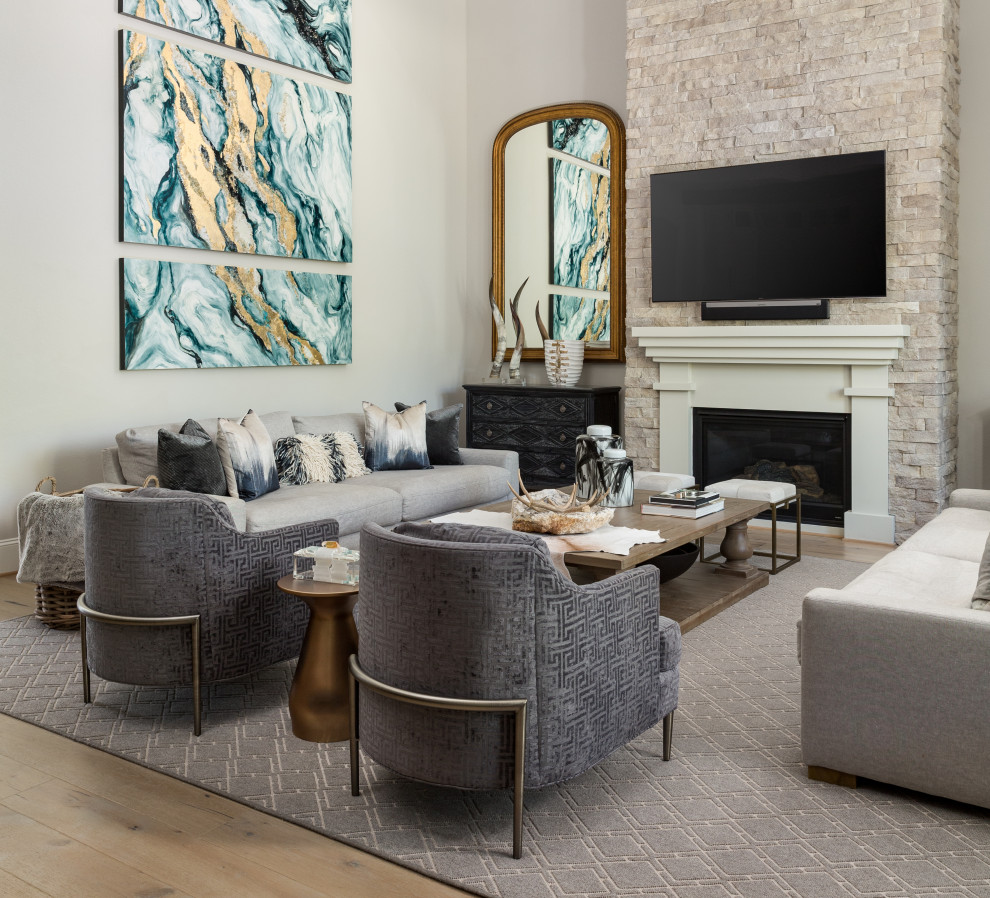 This is an example of a mid-sized transitional open concept living room in Houston with grey walls, light hardwood floors, a standard fireplace, a stone fireplace surround, a wall-mounted tv and brown floor.