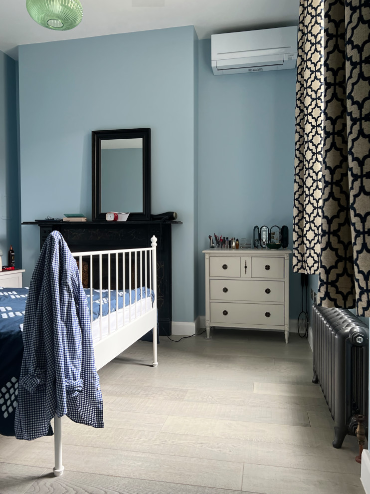 Modelo de dormitorio principal rural de tamaño medio con paredes azules, suelo de madera clara, estufa de leña y marco de chimenea de metal