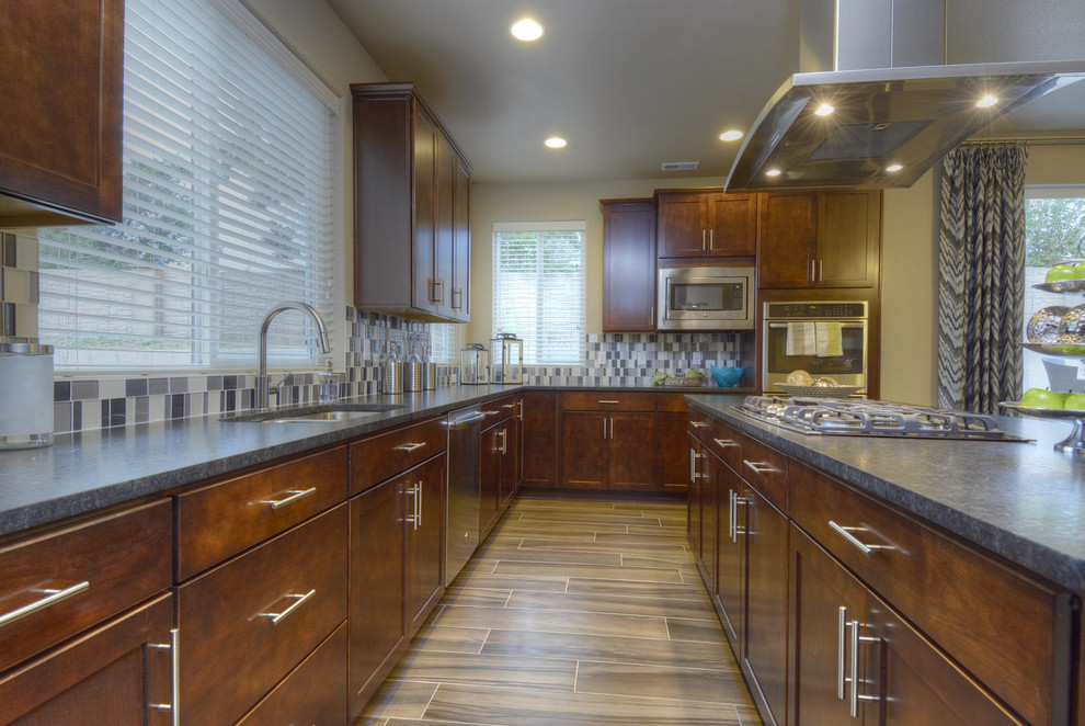 Photo of a contemporary eat-in kitchen in Denver with an undermount sink, recessed-panel cabinets, dark wood cabinets, granite benchtops, metallic splashback, glass tile splashback, stainless steel appliances, dark hardwood floors and with island.
