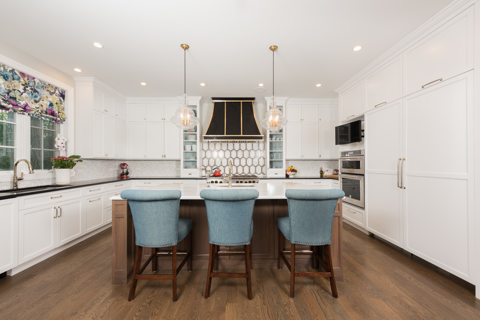 This is an example of a large transitional u-shaped kitchen in Chicago with an undermount sink, white cabinets, granite benchtops, porcelain splashback, with island, shaker cabinets, multi-coloured splashback, stainless steel appliances and dark hardwood floors.