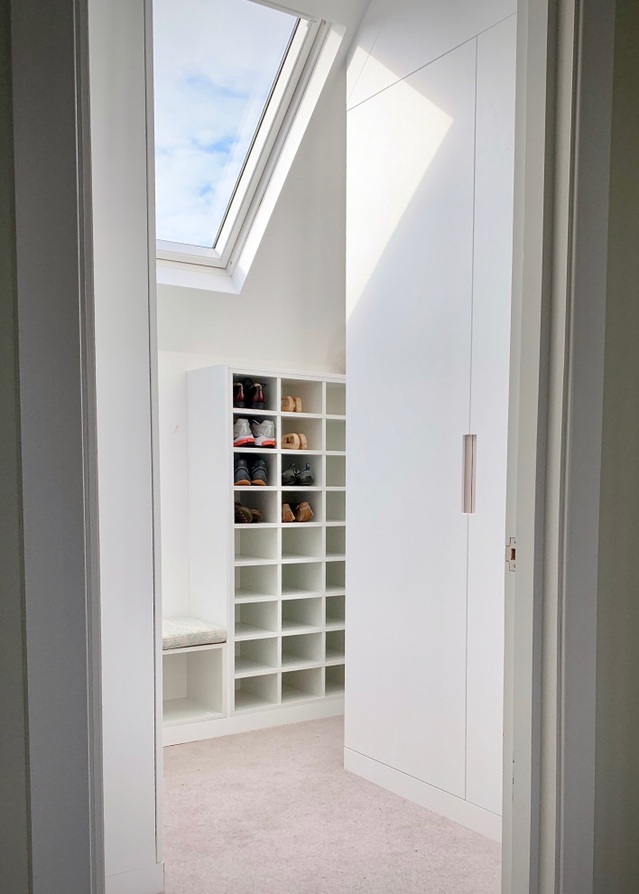 Ejemplo de armario vestidor unisex actual pequeño con armarios con paneles lisos, puertas de armario blancas, moqueta y suelo beige