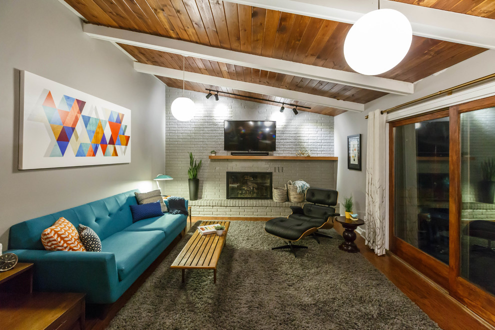 Photo of a mid-sized midcentury open concept family room in Grand Rapids with grey walls, medium hardwood floors, a standard fireplace, a brick fireplace surround and a wall-mounted tv.