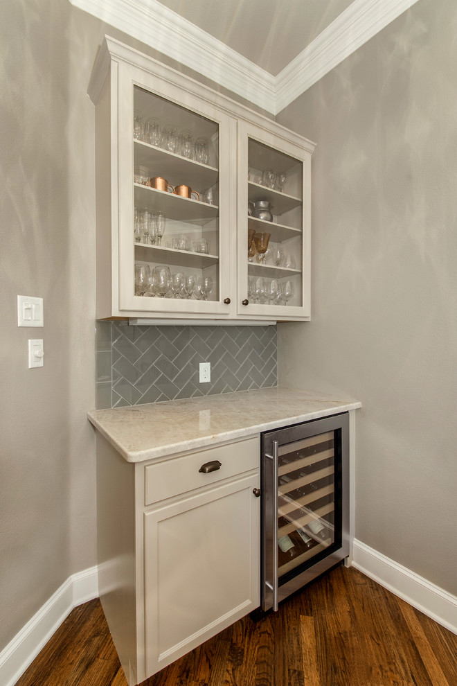 Inspiration for a mid-sized traditional l-shaped home bar in Dallas with white cabinets, granite benchtops, blue splashback, glass tile splashback, glass-front cabinets and medium hardwood floors.